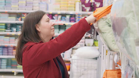 Woman in a mall chooses a warm blanket. The woman likes the bedding she smiles approvinglyの写真素材