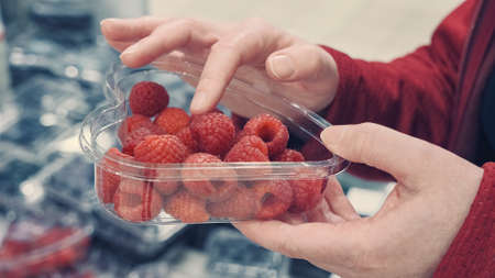 Women hands in the store, choose an large, ripe, red raspberries. Close up shot. The concept of shopping, vegetarianism, consumption of fruits and vitaminsの写真素材