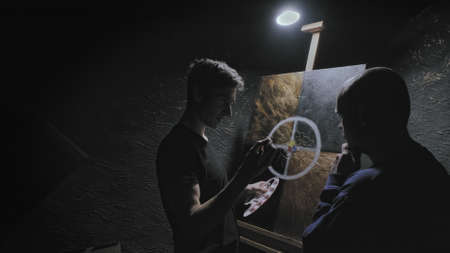 Master artist teaches man to paint. He explains in detail how to draw picture correctly. Student listens attentively. Concept of teaching visual arts, constructive criticism and adviceの写真素材