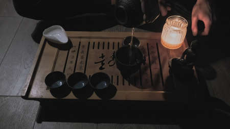 On the tea board is a clay Buddha figure and a candle. The tea master brews green tea pours it into cups. The concept of religion, hobbies, and lifestyleの写真素材