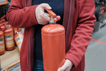 Woman in a store chooses for buy a small fire extinguisher. Concept of compliance with fire safety at home, in car and at work. Hands close up shotの写真素材