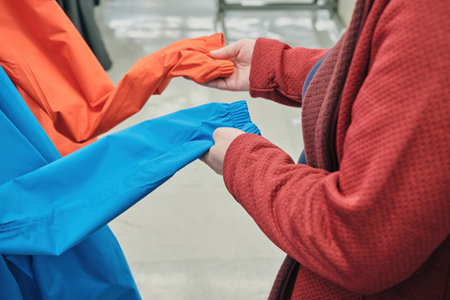 Caucasian woman wearing glasses and a mask against the virus chooses an blue and red windbreakers...