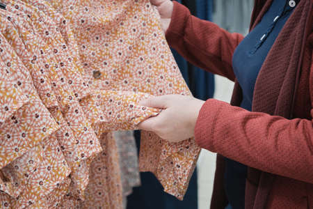 Pregnant woman chooses a loose dress in in a flower. Concept of buying new clothes, fashion, beauty and an active lifestyle while carrying child. Hands close up shotの写真素材