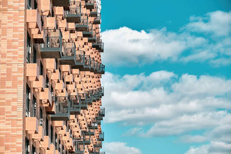 Part of the facade of a red, tiled, modern house. The house is ready for rent. Visible niches with wires for air conditioners. The background is a blue sky with white clouds. A clear dayの写真素材