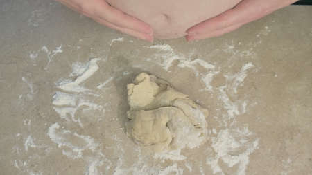 Fat chef with a bare stomach kneads baking dough on the table. Then he slaps his belly and wipes his hands on it. Concept of unsanitary conditions, parody and humor on bad cooks. Close upの写真素材