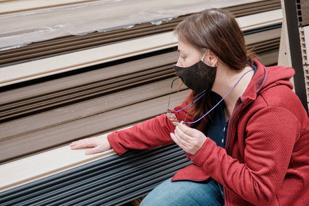 Woman wearing a mask against the virus is in a building materials store. She chooses the paneling...