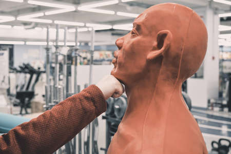 Woman in store chooses to buy red boxing mannequin in the form of man. She tries to hit him on the chin. Concept of women independence, feminism, gender equality and martial arts. Hands close up shotの写真素材
