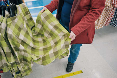 Pregnant woman chooses a roomy, green, flannelette plaid shirt in the store to buy. The concept of...