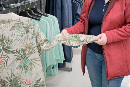 Overweight woman chooses a shirt with a tropical palm tree pattern at a clothing store to buy. The...