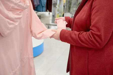 Caucasian woman chooses pink windbreaker jacket from the rain in store to buy. The concept of fashion and wardrobe updates. Hands close upの写真素材