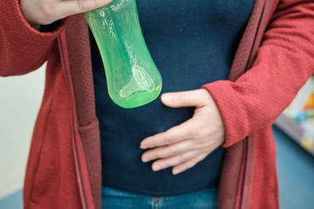 Pregnant girl in the store chooses a bottle with a pacifier for feeding the unborn baby. Concept of waiting for a child, motherhood and preparing for replenishment of family. Hands close up shotの写真素材
