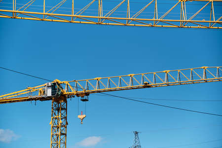 Yellow arrows of a construction crane on the background of electric wires and blue skyの写真素材