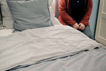 Tired woman sits in the evening in the bedroom next to the bed. The concept of fatigue at work and...