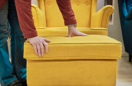 Caucasian woman in a store chooses for buy a chair and a footstool made of yellow fabric. The...