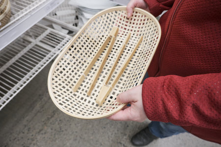 Caucasian girl buys wooden, wicker bread dishes with wooden tongs in a store. The concept of buying new dishes and kitchen equipment. Hands close up shotの写真素材