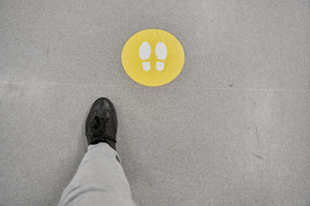 Man in black shoes and white pants follows the signs on the floor of a mall. The concept of...