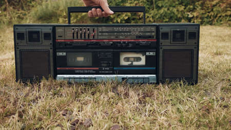 There is an old retro tape recorder on grass. Woman picks up the device by handle. Concept of old school vintage technique of the last centuryの写真素材