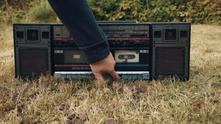 There is an old retro tape recorder on grass. Woman presses play button. Concept of old school vintage technique of the last centuryの写真素材