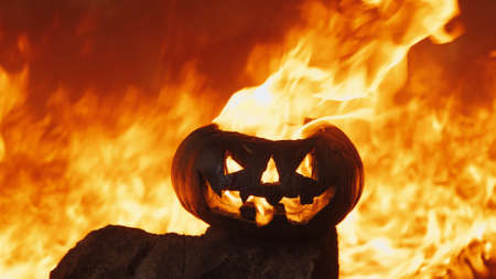 Halloween pumpkin, fiery flame burns inside it. Behind it, ignites with wall of hellfire. Concept of holiday of night of all saints and scary dark fairy talesの写真素材