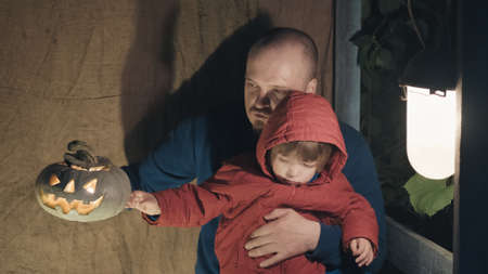 Father and daughter are sitting on porch of village house and playing with pumpkin for Halloween. Candles are burning inside pumpkin. Concept of feast of the night of all Saints and family relationsの写真素材