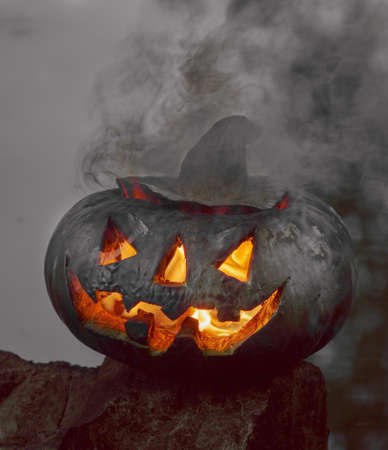 Halloween. A pumpkin on the background of a pond, it glows, a fiery flame burns inside it. The concept of the holiday of the night of all saints and scary dark fairy tales in the autumn harvest seasonの写真素材