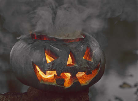 Halloween. A pumpkin on the background of a pond, it glows, a fiery flame burns inside it. The concept of the holiday of the night of all saints and scary dark fairy tales in the autumn harvest seasonの写真素材