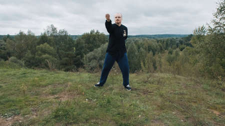 Middle aged Caucasian man practices wushu in the summer in a park on a hill. Traditional Chinese gymnastics qigong and Tai chi. Meditation and relaxation in nature. Healthy lifestyle and sportsの写真素材