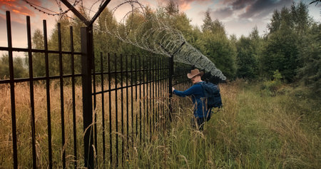 Man runs to the fence with barbed wire and climbs on it. Evening sunset. The concept of illegal border crossing, penetration into a protected object and unlawful migrationの写真素材