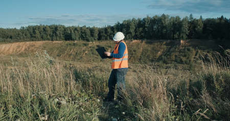 Working engineer in a white helmet next to a sand pit. The concept of mining, construction and...
