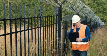 Worker with a measuring tape measure a fence with barbed wire. The concept of border closure, districts and specially protected objects. Access restriction and protectionの写真素材