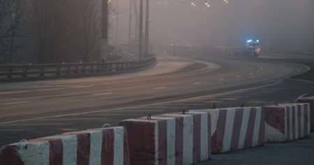Night, thick fog over highway. Part of road is lockdown with concrete blocks. Ambulance with sirens is moving away in distance. Concept of blocked and prohibition of movement in a state of emergencyの写真素材