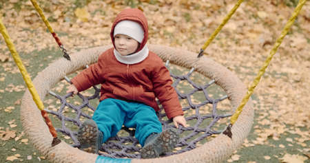 Small, cute child rides on a swing in the yard on a walk. The carousel rolls the baby. Lifestyle and active recreationの写真素材