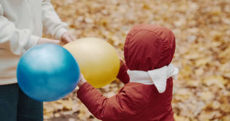 Small, cute child is playing with his mother in inflatable balloons. The concept of childhood, happy family and lifestyle. Autumn nature, clean air, active holidays on weekendsの写真素材