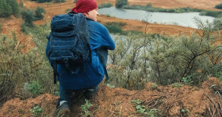 Hiker walks with a backpack in a large, sandy quarry at sunset. The quarry is overgrown with grass and trees. The concept of hiking a healthy lifestyle and weekends in the fresh air. There water belowの写真素材
