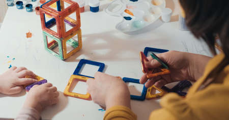 Child with his mother collects a magnetic constructor, a close up shot, a rear view, no faces are...