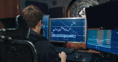 Man trader, freelancer on stock exchange trades options computer, charts of growth and fall of quotations on screen, home environment. Concept of playing on stock, futures and bonds trading exchangeの写真素材