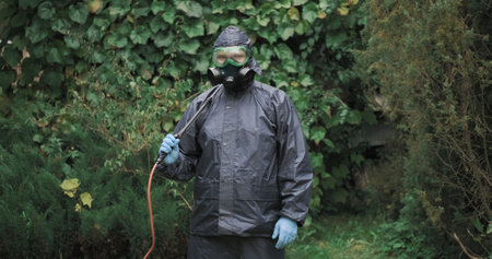 Man in a chemical protection suit, a respirator, glasses for eye protection, medium shot. Concept of disinsection and treatment of plots, houses against pests, termites, mold and parasitesの写真素材