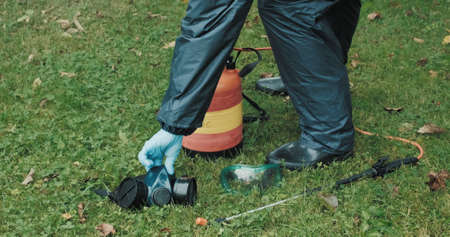 Lawn treatment with insecticides and toxins from ixodic mites and other blood sucking parasites. A man in a protective suit sprays poison on the grassの写真素材