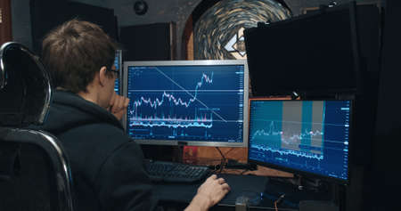 Man trader, freelancer on stock exchange trades options computer, charts of growth and fall of quotations on screen, home environment. Concept of playing on stock, futures and bonds trading exchangeの写真素材