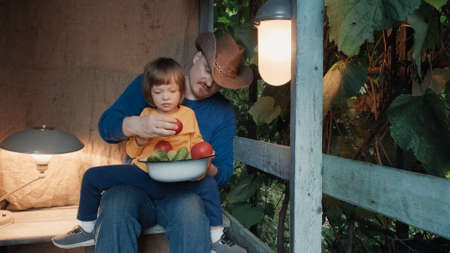 Father cowboy and small child eat fresh, organic vegetables from a farm sitting on porch of a country farm. The concept of healthy bio organic food and natural products without pistecides and nitratesの写真素材