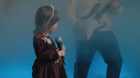 Little girl on stage in vintage dress, she sings into microphone and dances, her father plays an...