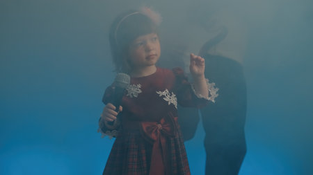 Little girl on stage in vintage dress, she sings into microphone and dances, her father plays an electric guitar. Color music is shining and smoke is billowing. Family time, creativity and hobbiesの写真素材
