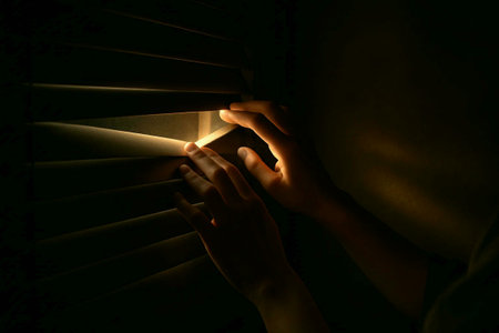 Close-up of woman's hands peeking through the blindsの素材