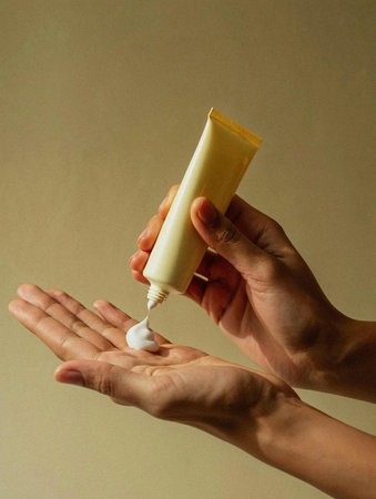 Female hands holding a tube of cream on a beige background.の素材