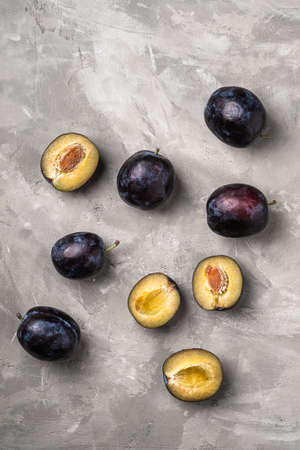 Fresh ripe plum fruits whole and sliced with water drops on stone concrete background, top viewの写真素材