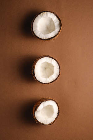 Three coconut fruits in row on brown plain background, abstract food tropical concept, top view