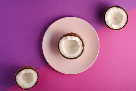 Coconut half in pink plate with nut fruits on violet and purple plain background, abstract food...