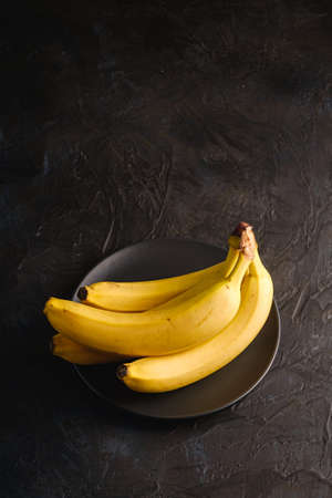 Banana fruits in black plate on dark textured background, angle view copy spaceの写真素材