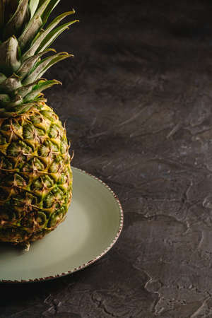 Fresh sweet pineapple in grey plate on dark black textured background, angle view, croppedの写真素材