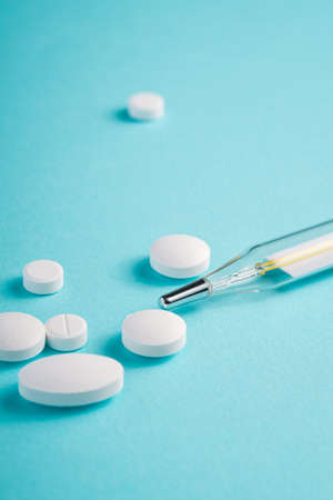 Pills, tablets and analog thermometer on bright blue background, healthcare medical concept, antibiotics and cure, angle view macroの写真素材